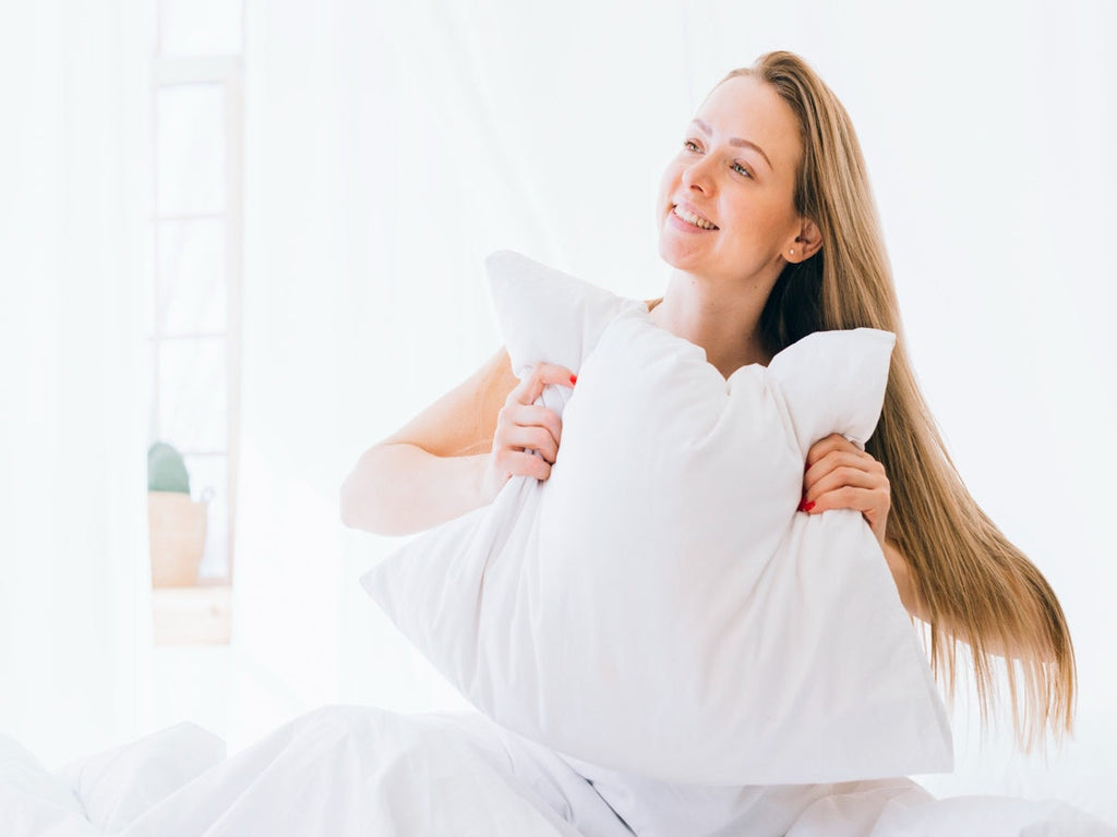 Woman holding a pillow in bed, representing when to replace your pillow for better sleep quality