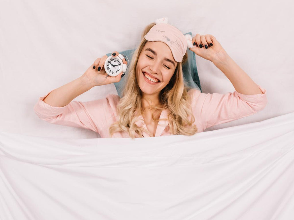 Woman waking up refreshed with an alarm clock, symbolising resetting your sleep schedule in January